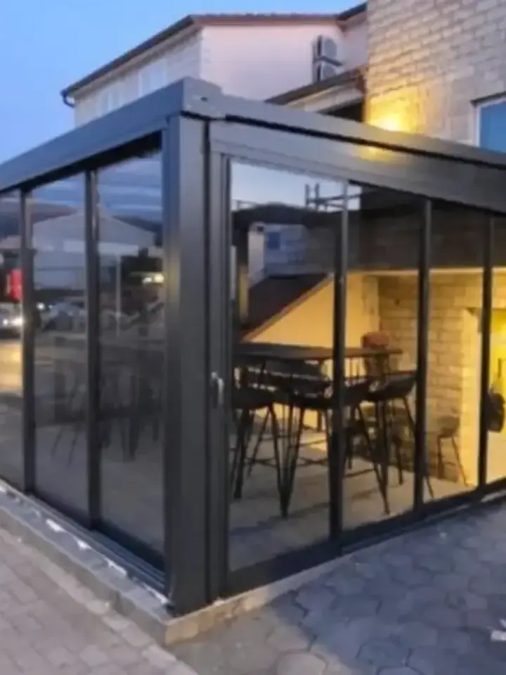 Ostakljena bašta kafića u crnim aluminijskim profilima, uveče, s upaljenim svjetlom unutra